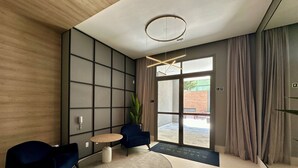 Eine moderne Lobby mit einer Holzwand, einer großen Glastür, zwei blauen Stühlen, einem runden Tisch und einer Deckenleuchte.