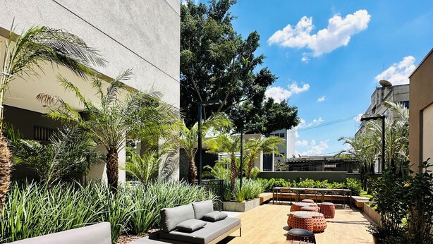 Ein moderner Außenbereich mit Sofas und runden Tischen, umgeben von Pflanzen und blauem Himmel.