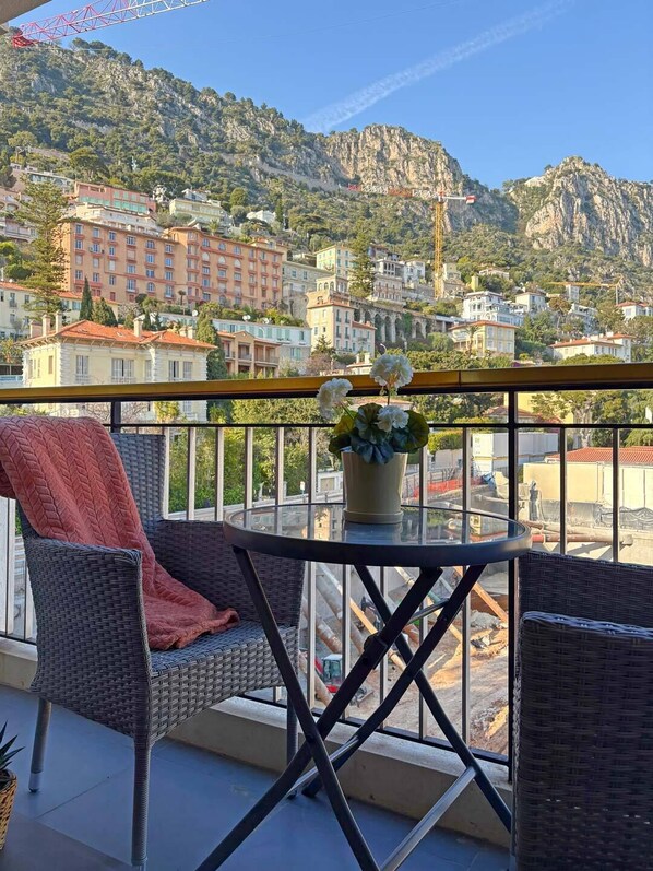 Un balcon avec des fauteuils en osier, une table et un pot de fleurs.