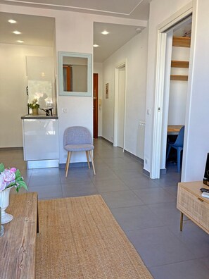 A modern living room with a sofa, a small table, and a kitchen area with a sink and a mirror. - Charming Apartment with Balcony & Mountain Views in Beaulieu-sur-Mer (Beaulieu-sur-Mer)