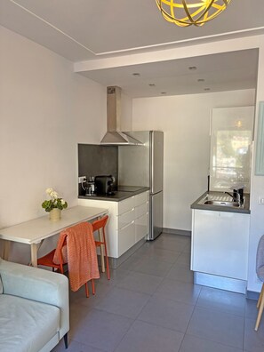 Une cuisine compacte équipée d’un réfrigérateur, d’une cuisinière et d’un évier. On y trouve également un coin repas avec une table et des chaises, ainsi qu’un canapé dans l’espace de vie attenant.