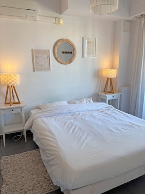 A bedroom with a large bed, two bedside tables with lamps, a wall-mounted mirror, and framed artwork. - Charming Apartment with Balcony & Mountain Views in Beaulieu-sur-Mer (Beaulieu-sur-Mer)