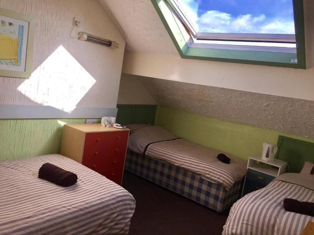 A dormitory room with two beds, a small desk, a dresser, and a skylight.