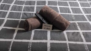 A bed with a checkered bedspread, two pillows, a rolled towel, and a thank you card. - The Galloway Hotel  (Blackpool)