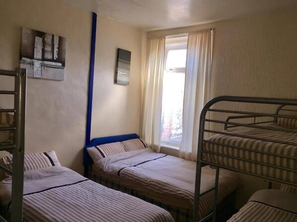 A dormitory room with bunk beds, a window with curtains, a wall-mounted shelf, and a mirror.