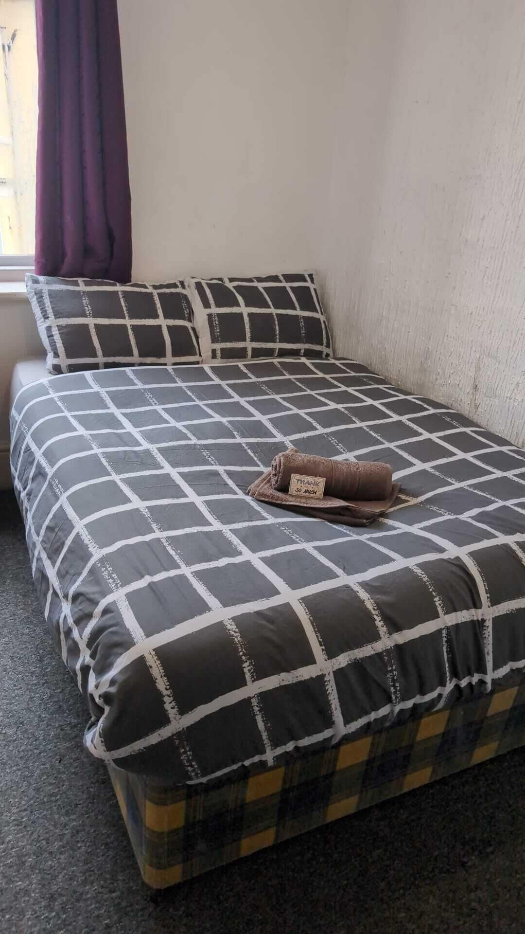 A bed with a checkered bedspread, a folded towel, and a window with curtains.