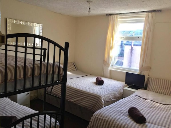 A room with bunk beds, a television, a window with curtains, and a mirror on the wall.