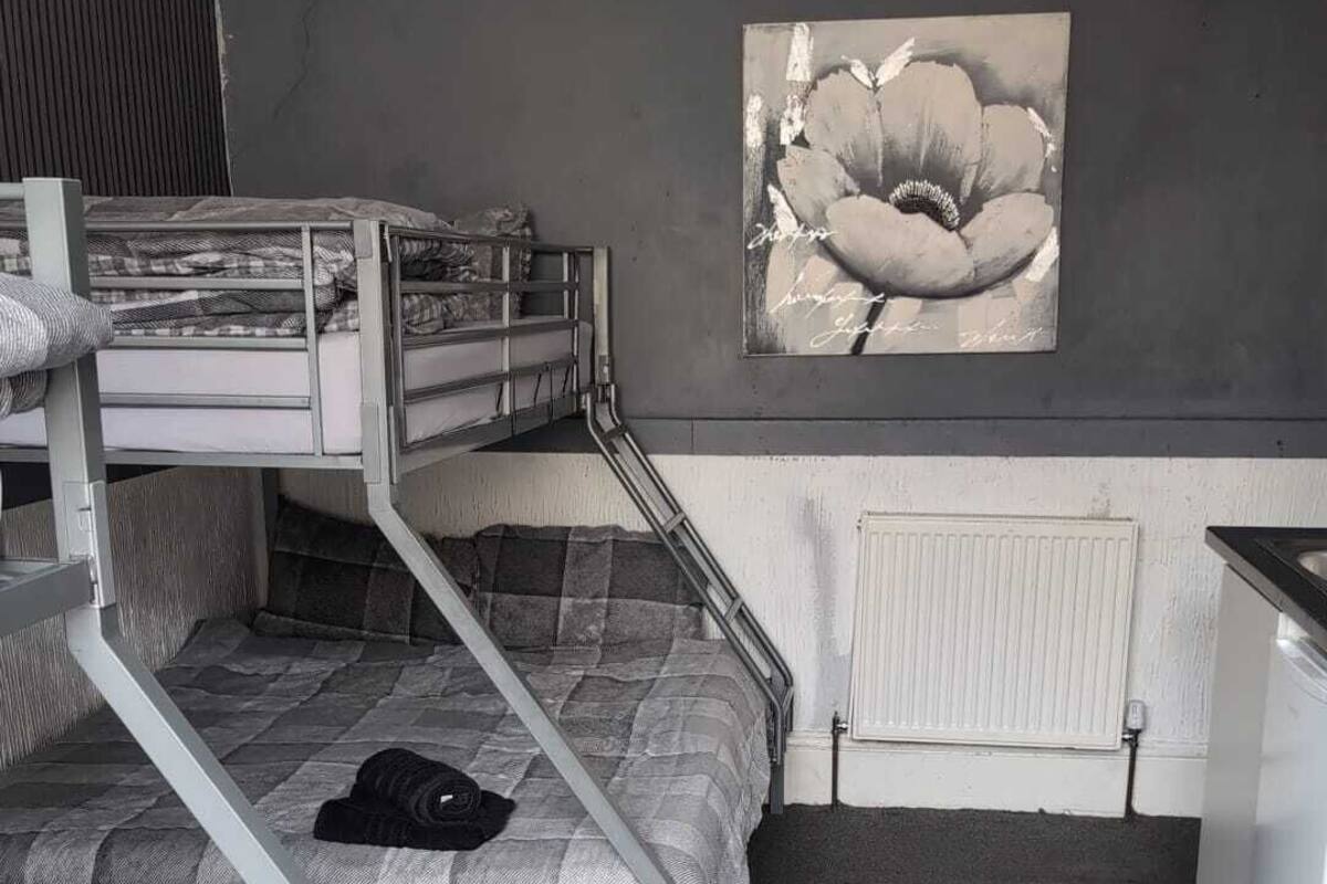 A dormitory room with bunk beds, a radiator, a wall-mounted artwork, and a small kitchenette.