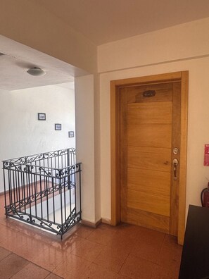 A hallway with a wooden door, a metal railing, and a tiled floor. - 301 - Cozy colonial unit with rooftop terrace. (Santo Domingo)