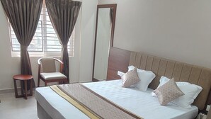 A hotel room with a large bed, a chair, a small table, an air conditioning unit, and a mirror.