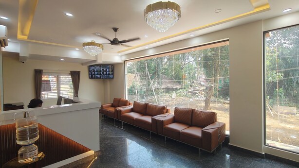 A reception area with a sofa, a TV, a ceiling fan, and a large window with a view of greenery.