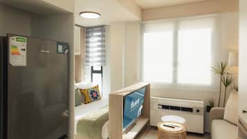 A modern living room with a flat-screen TV, a sofa, a small table, and a window with blinds.