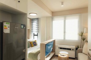 A modern living room with a flat-screen TV, a sofa, a small table, and a window with blinds. - TEN on V - Fluent Serviced Apartments (Cape Town)