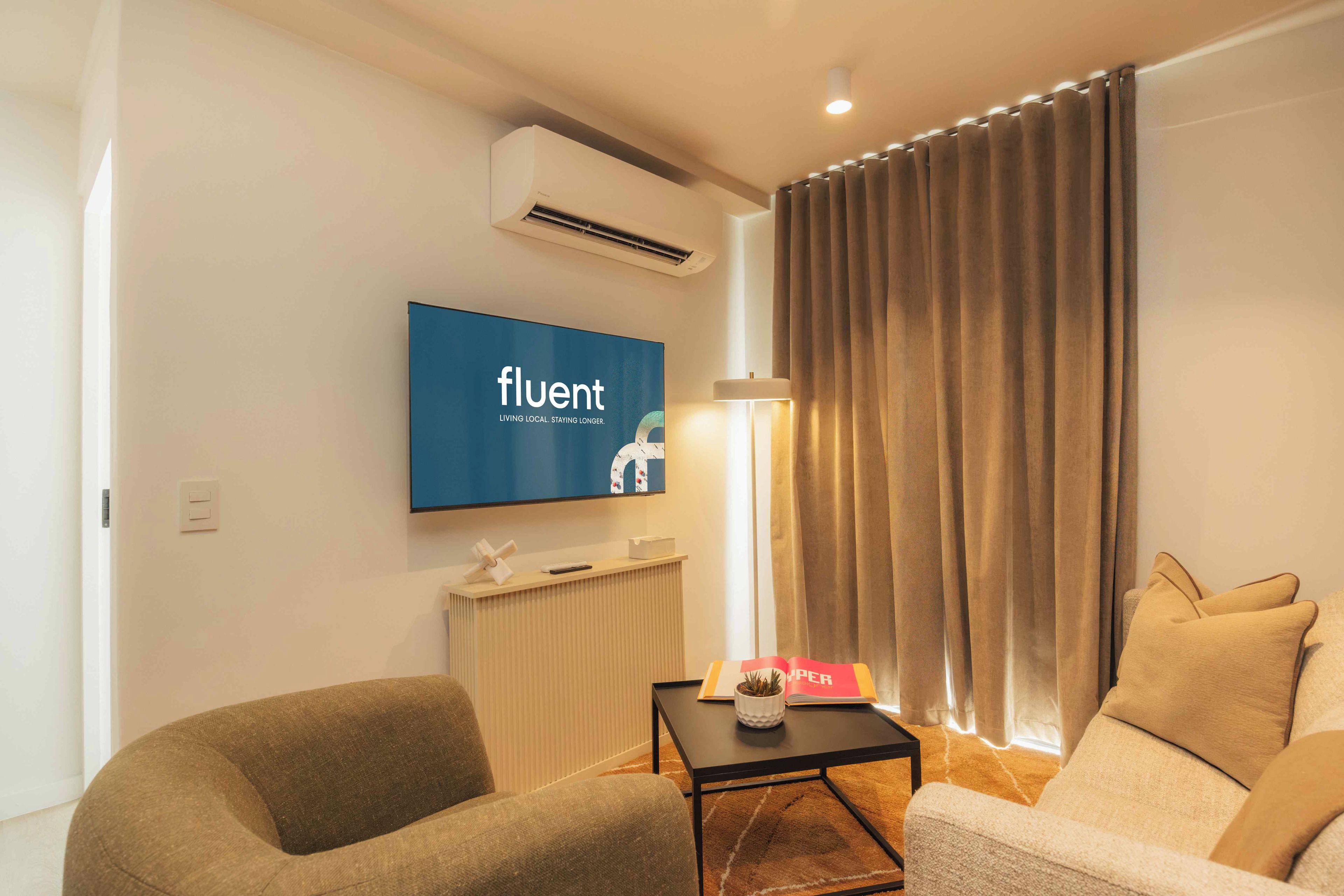 A modern living room with a flat-screen TV mounted on the wall, a standing lamp, and two sofas.