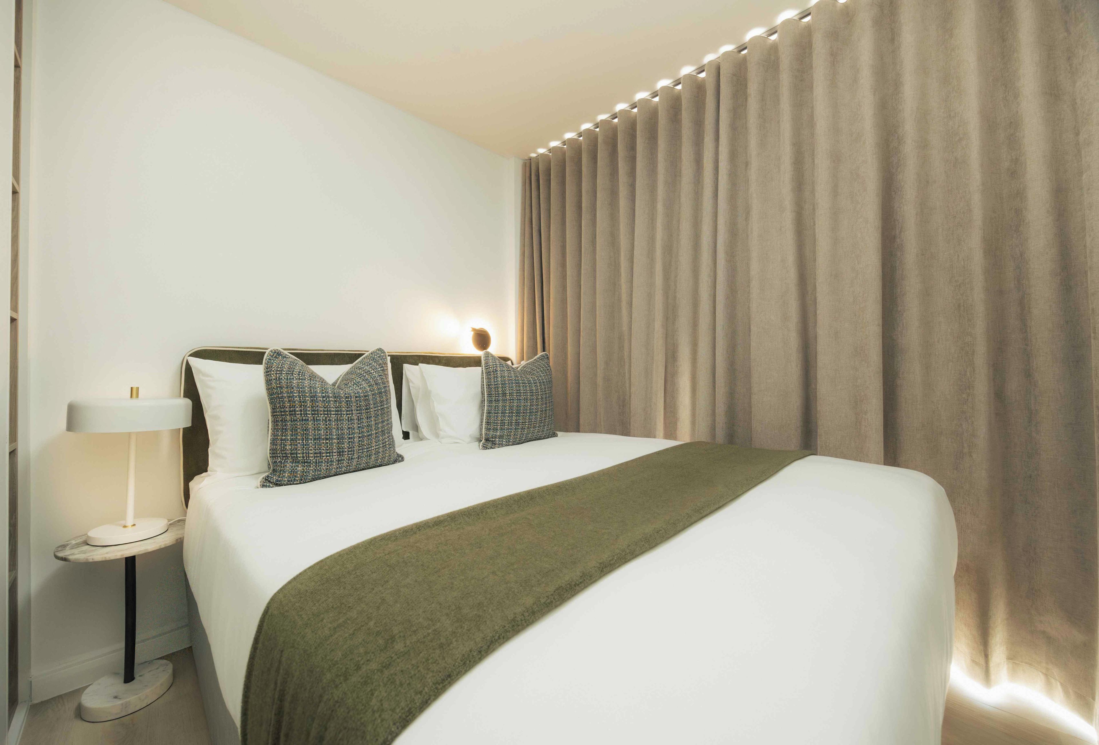 Una camera d'albergo con un letto, una lampada da comodino e una tenda.