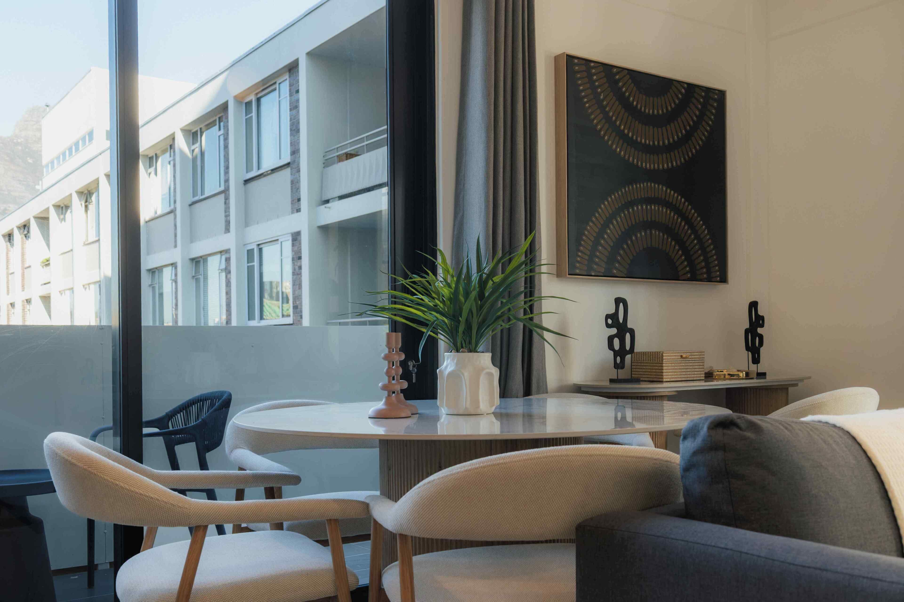 Un interior moderno con una mesa redonda, dos sillas, un sofá, una planta en maceta y una obra de arte colgada en la pared.