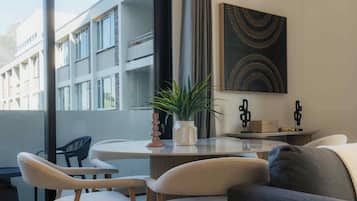 A modern interior with a round table, two chairs, a sofa, a potted plant, and a wall-mounted artwork.