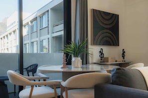 Een modern interieur met een ronde tafel, twee stoelen, een bank, een potplant en een kunstwerk aan de wand.