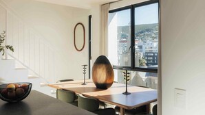 A modern dining area with a table, chairs, and a view of a cityscape through a large window. - TEN on V - Fluent Serviced Apartments (Cape Town)