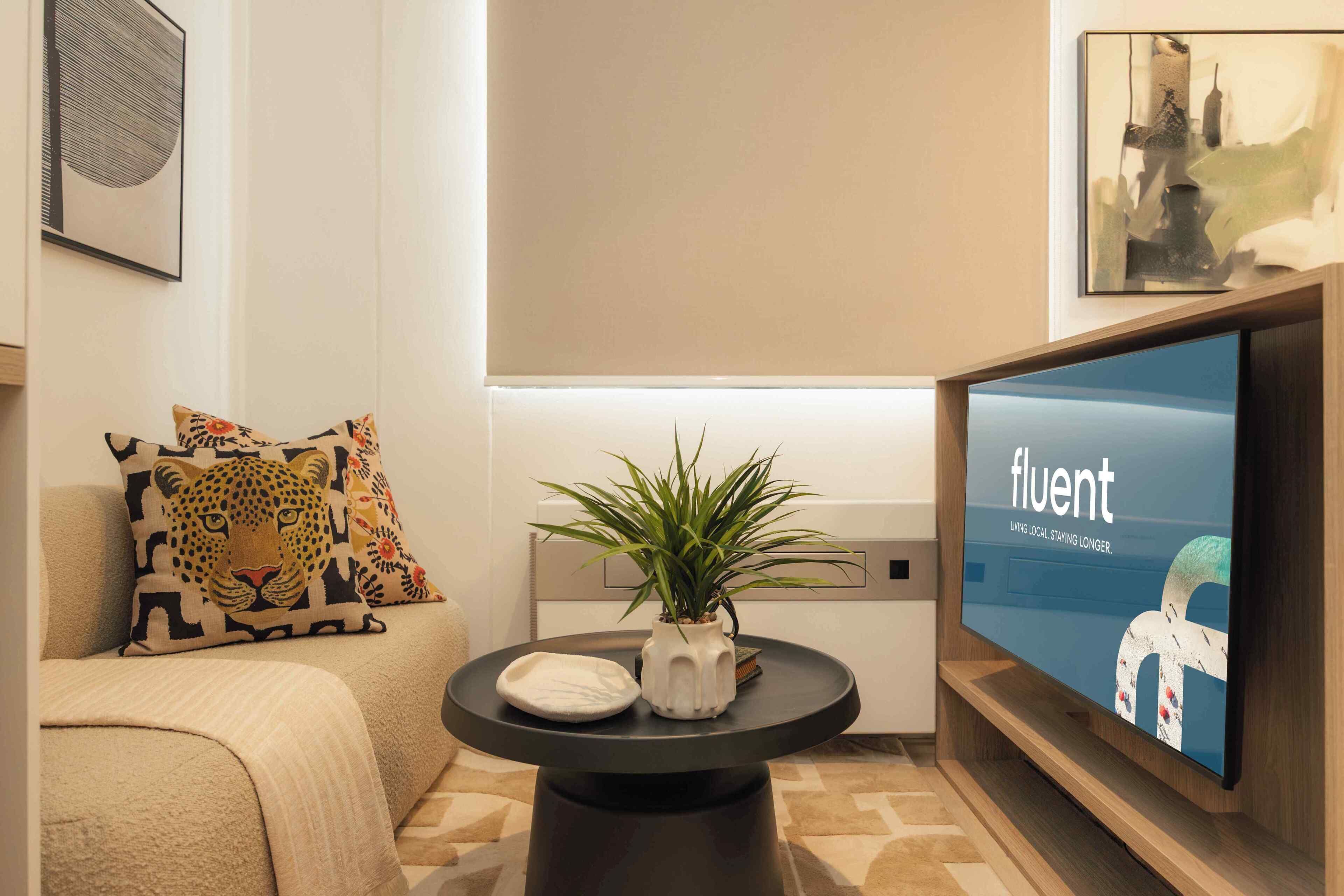 Una sala de estar moderna con un sofá, almohadones decorativos, una mesa redonda con una planta y un televisor que muestra la palabra 'fluent'.