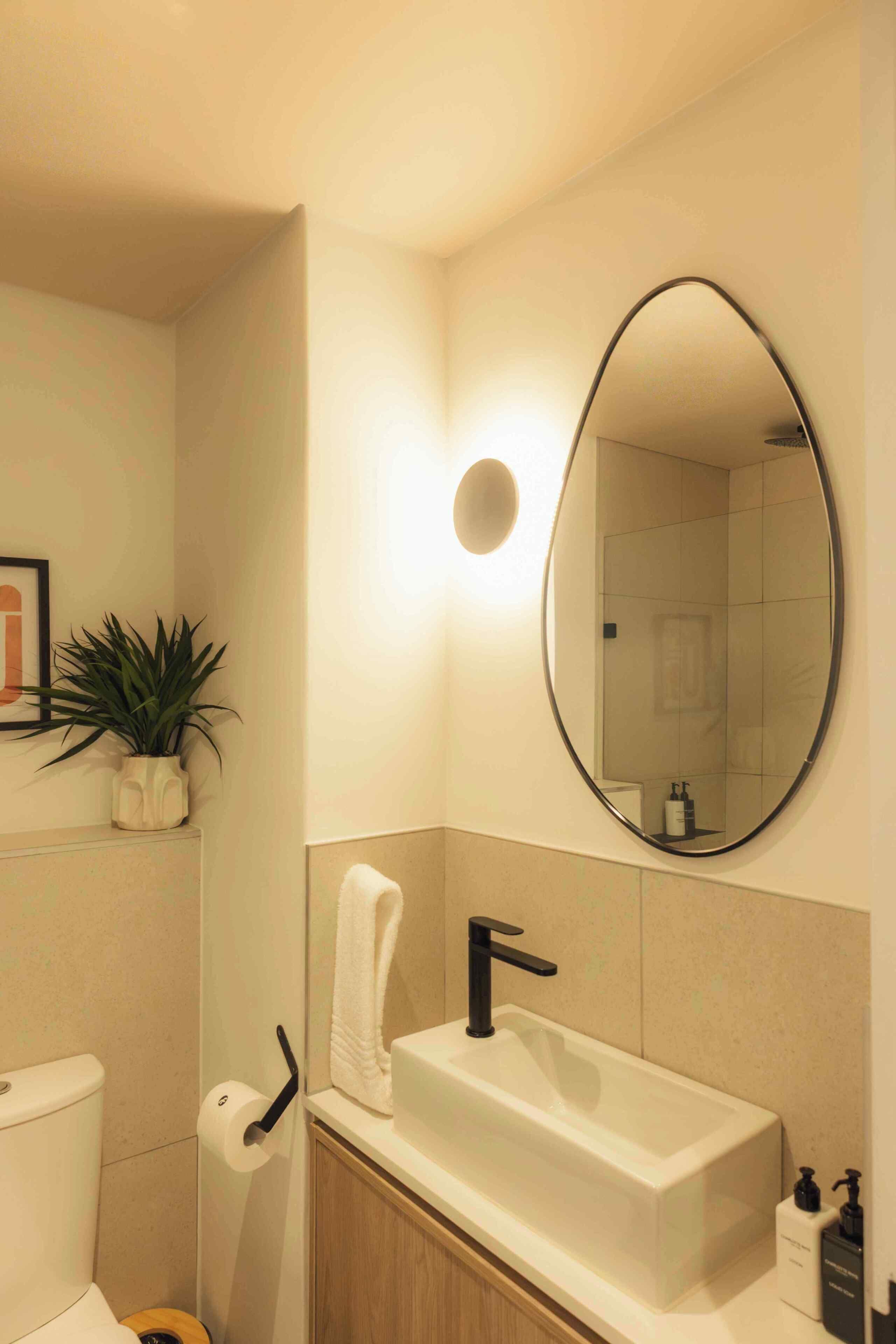 A bathroom with a white sink, a black faucet, a round mirror, a towel hanging on a rack, a toilet, and a potted plant.