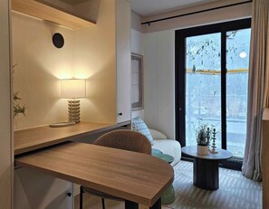 Een moderne hotelkamer met een houten bureau, een ronde tafel, een bank en uitzicht op een besneeerd landschap.