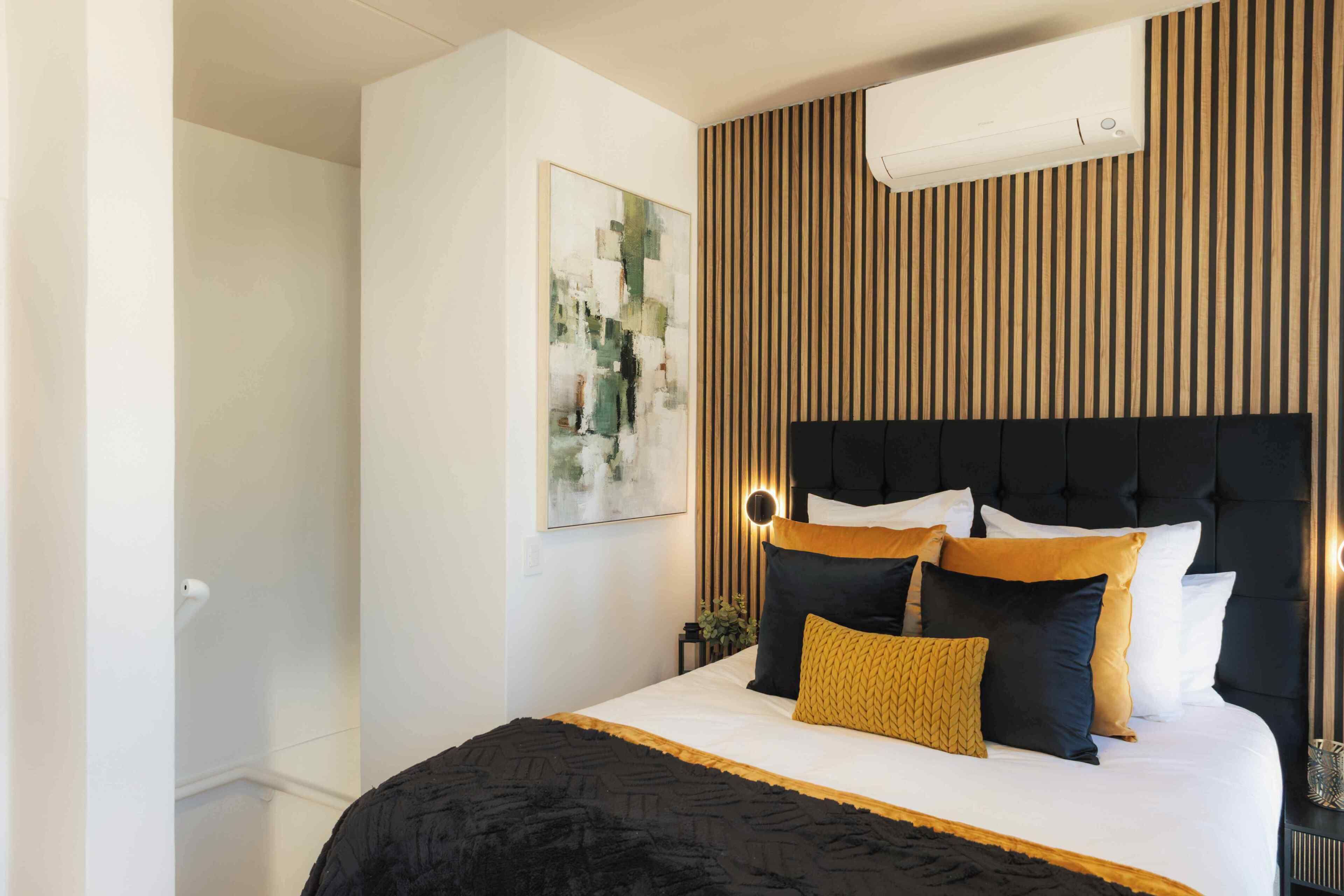 Un dormitorio moderno con una cama grande, un cabecero con luces, aire acondicionado instalado en la pared y una obra de arte abstracta.