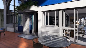 Een modern buiten zitgedeelte met een ronde tafel en stoelen, een betonnen pilaar met de tekst 'COLLECT HERE', en een glazen deur met 'WELCOME' aanduiding.