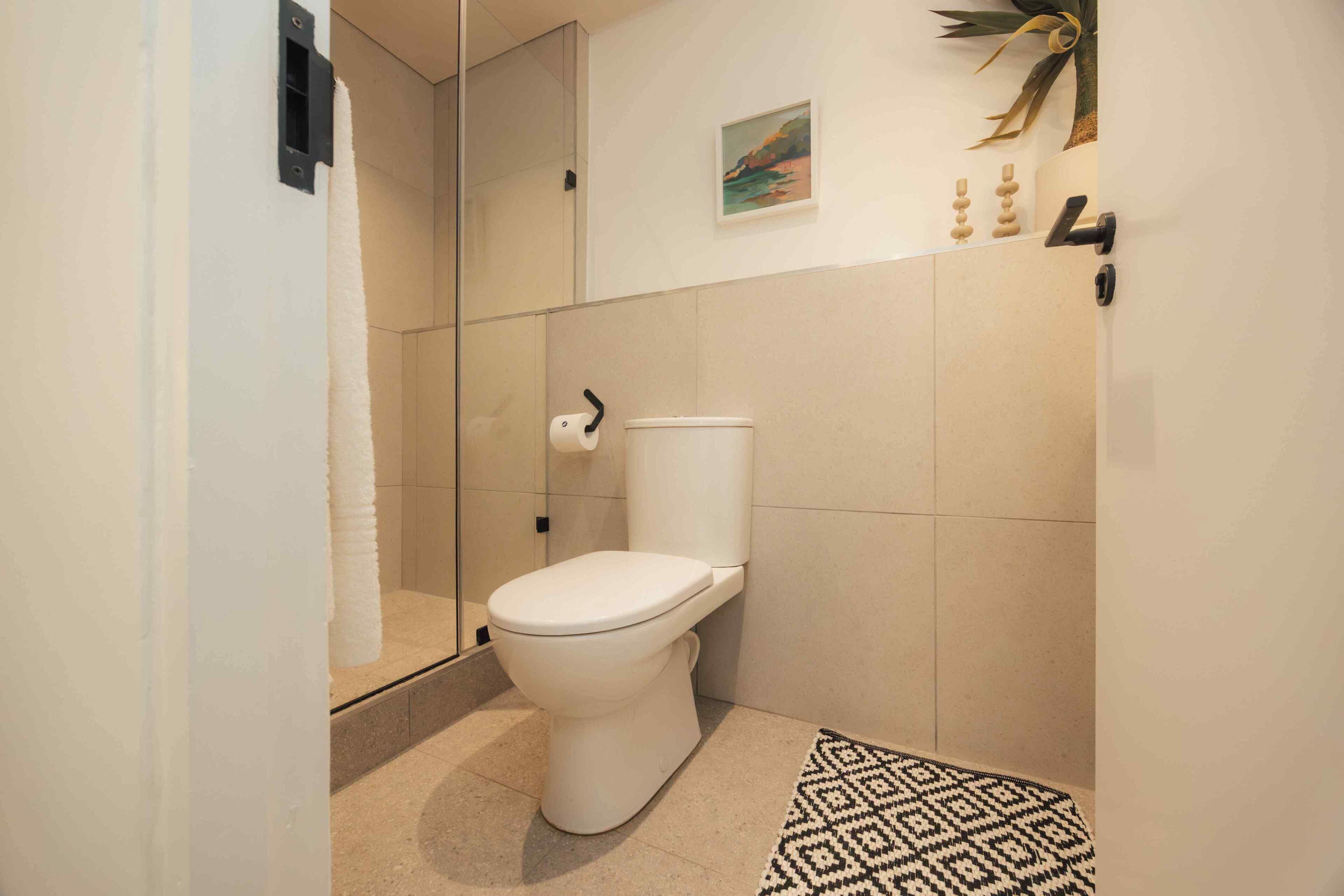 A modern bathroom with a toilet, a shower area, and a patterned rug.