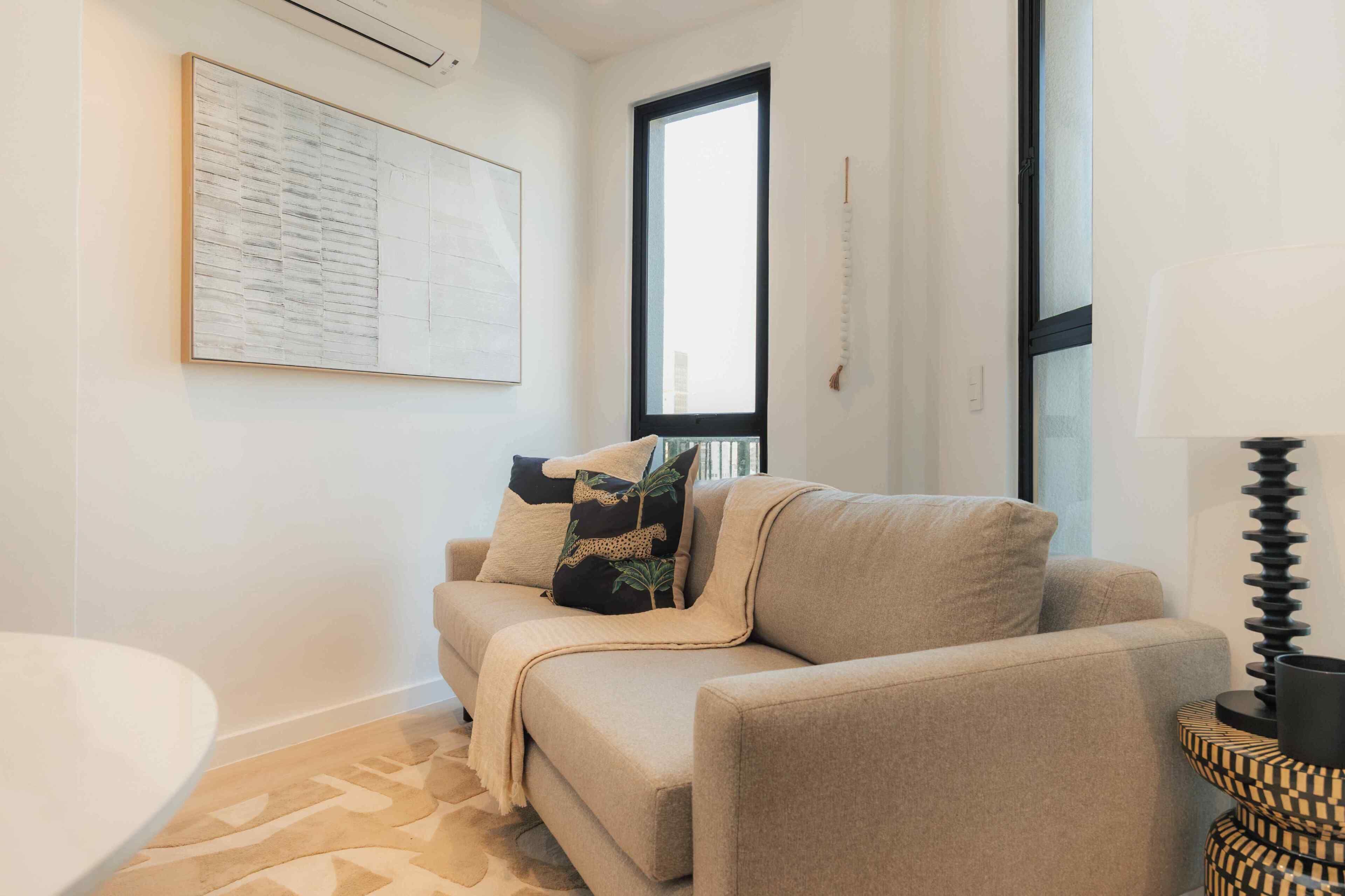 Una sala de estar con un sofá color beige, una mesa redonda, un ventanal grande y un aire acondicionado instalado en la pared.