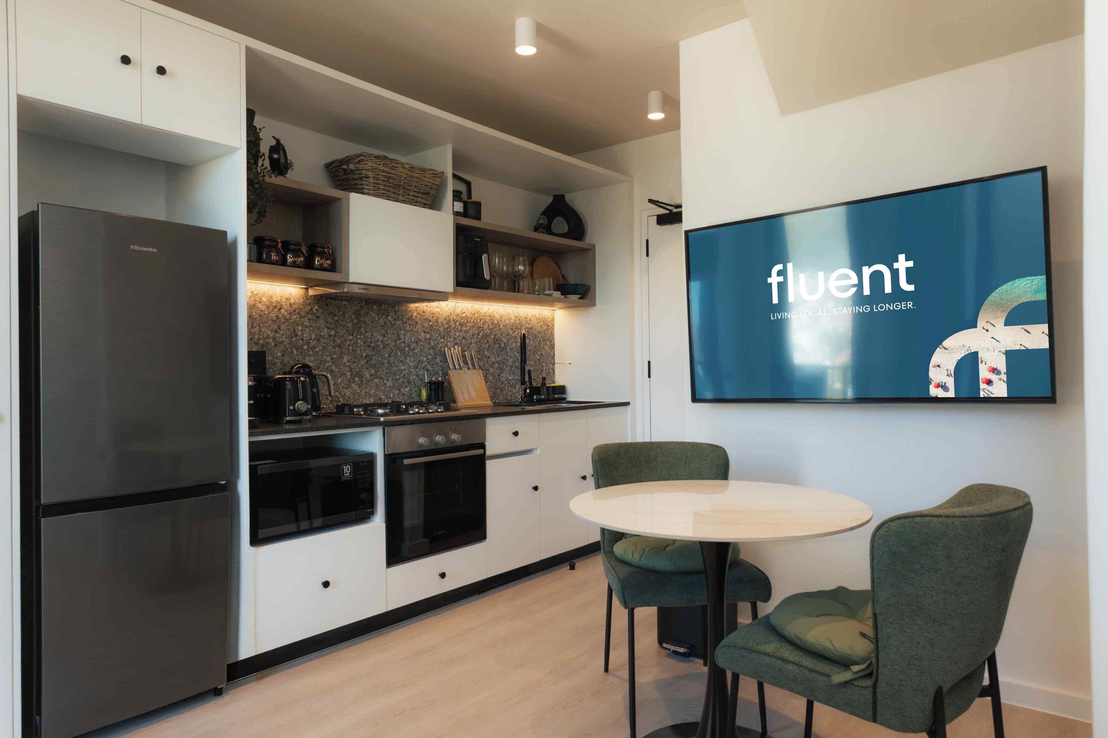 A modern kitchen with a built-in oven, a refrigerator, and a dining area with two chairs and a table.