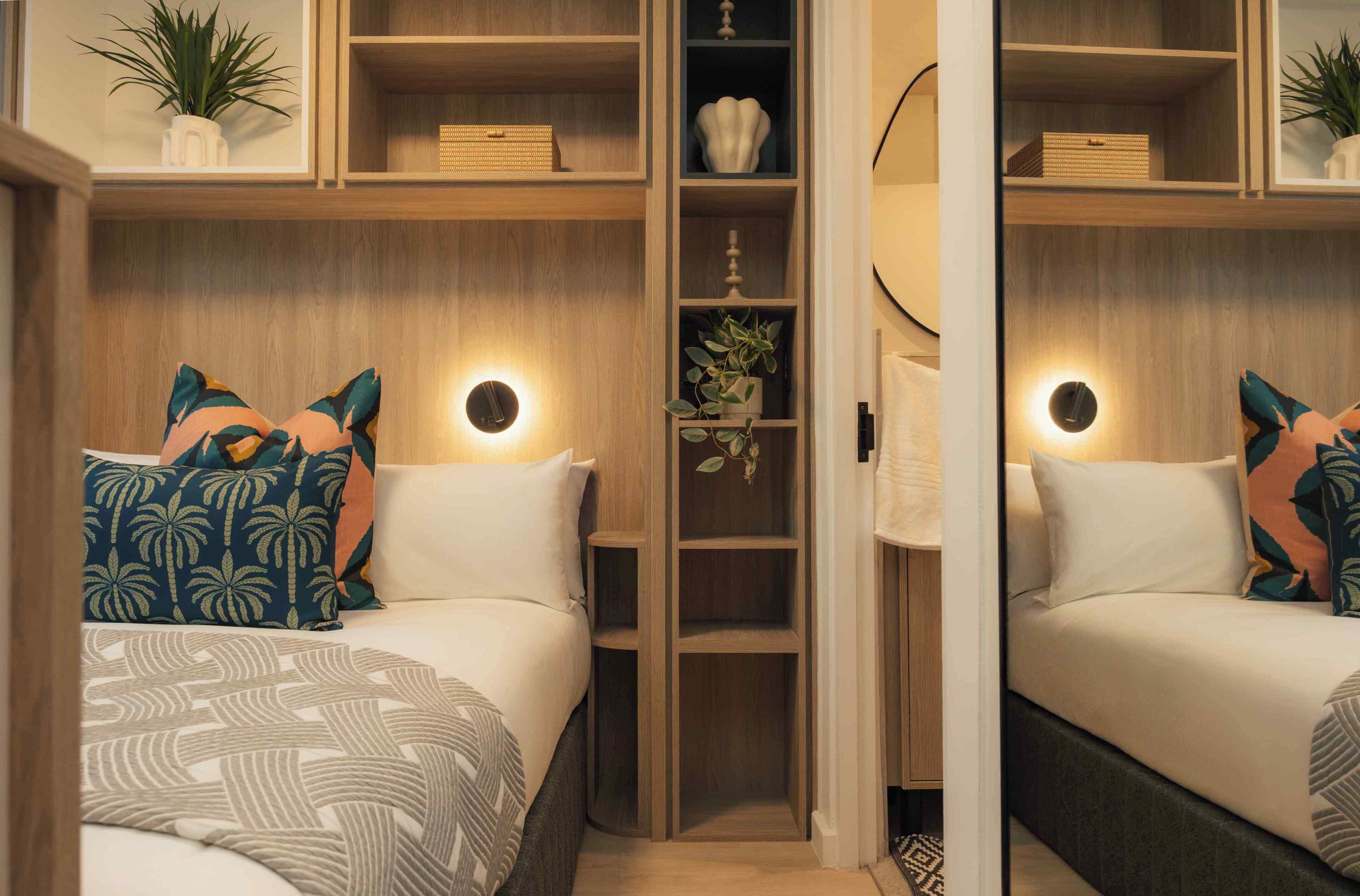 A bedroom with a bed, pillows, a nightstand, a bedside table, a wardrobe, and a mirror.