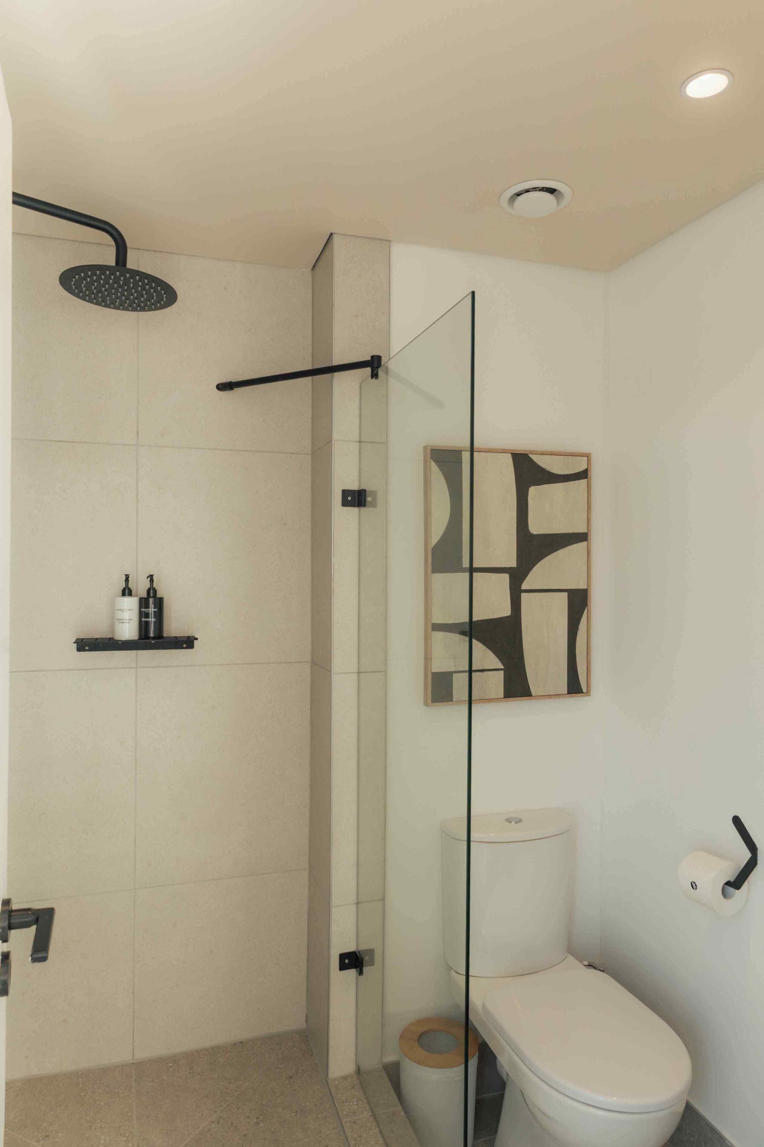 A modern bathroom with a glass shower enclosure, a toilet, and a shelf with toiletries.
