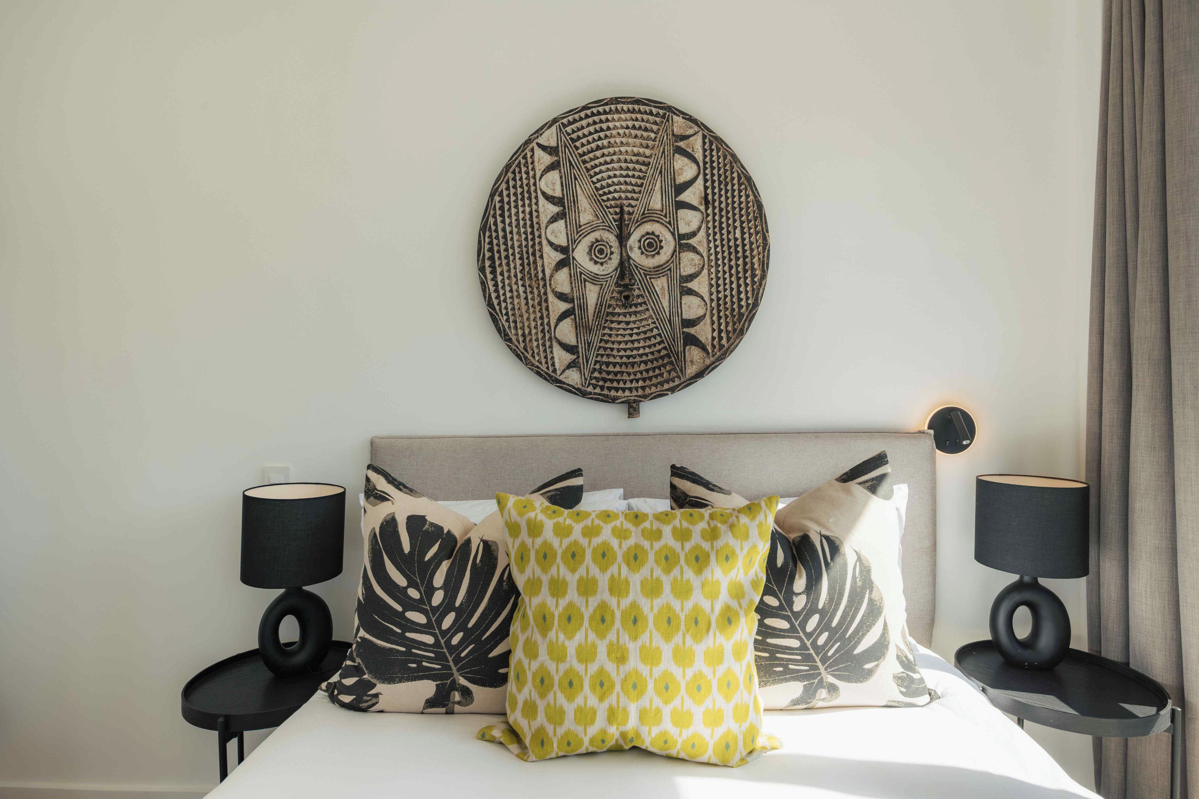 A bed with a headboard, two bedside tables, and a wall-mounted decorative piece.