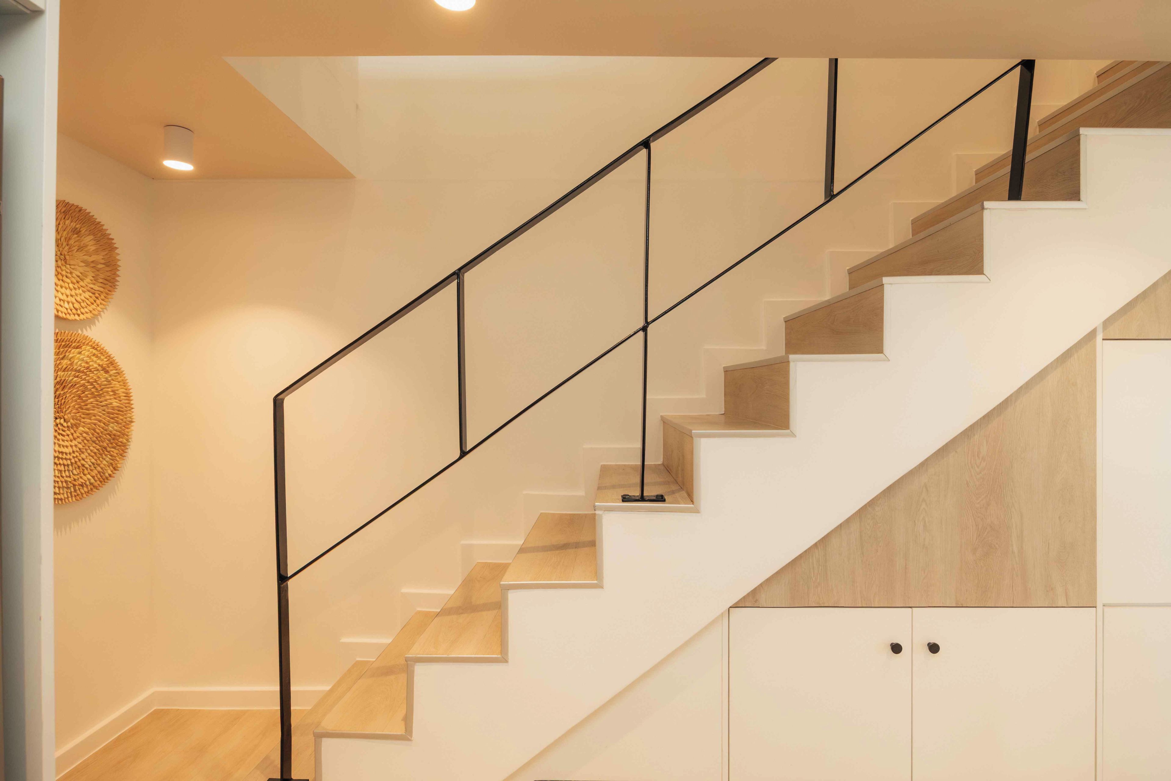A staircase with a wooden finish, white walls, and a black railing.