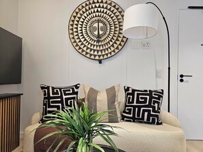 Une chambre à coucher moderne avec un élément de décoration circulaire au mur, deux coussins à motifs, une lampe sur pied et une plante en pot.