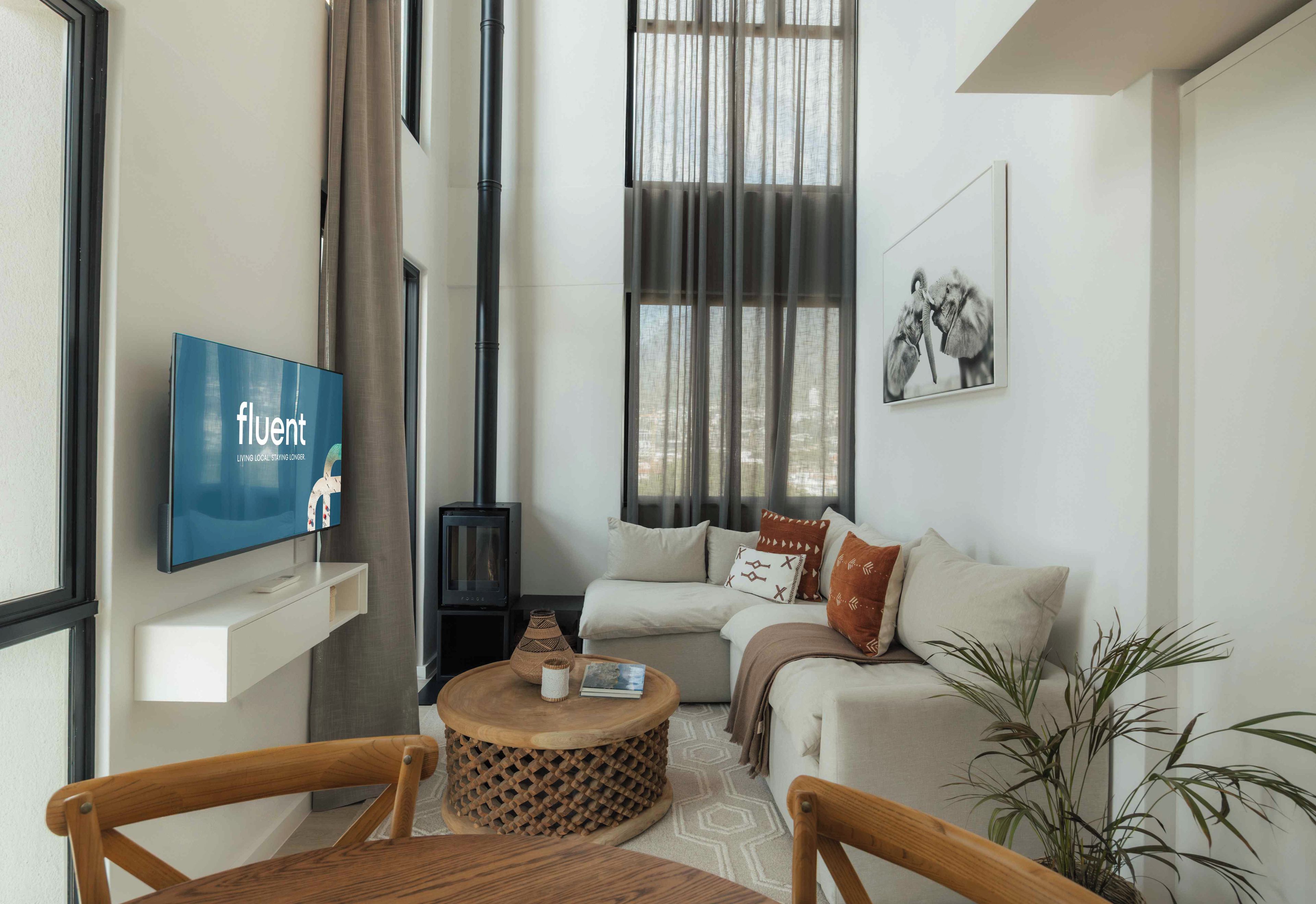 Una sala de estar moderna con una televisión de pantalla plana, un conjunto de sofás, una chimenea y un amplio ventanal con cortinas.