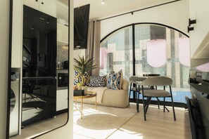 A modern living room with a sofa, chairs, a coffee table, and a large window with a view of buildings. - TEN on V - Fluent Serviced Apartments (Cape Town)