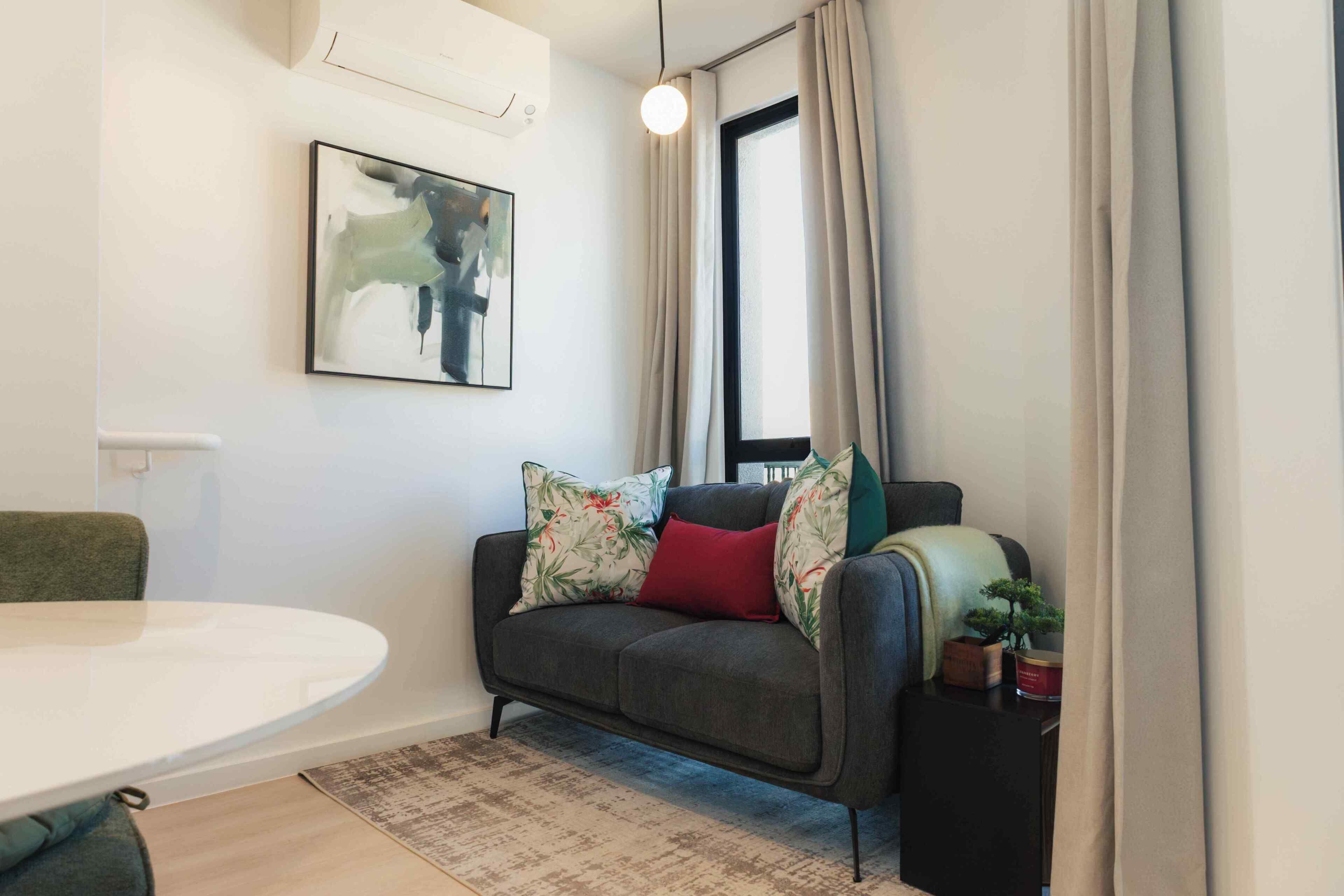 Una sala de estar moderna con un sofá gris, una mesa redonda, un cuadro en la pared y una ventana con cortinas.