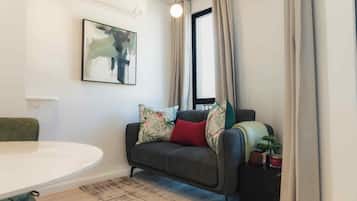 Una sala de estar moderna con un sofá gris, una mesa redonda, un cuadro en la pared y una ventana con cortinas.