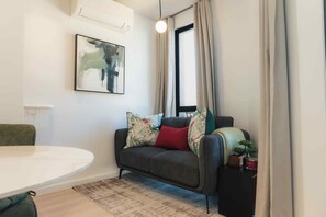 A modern living room with a grey sofa, a round table, a painting on the wall, and a window with curtains. - TEN on V - Fluent Serviced Apartments (Cape Town)