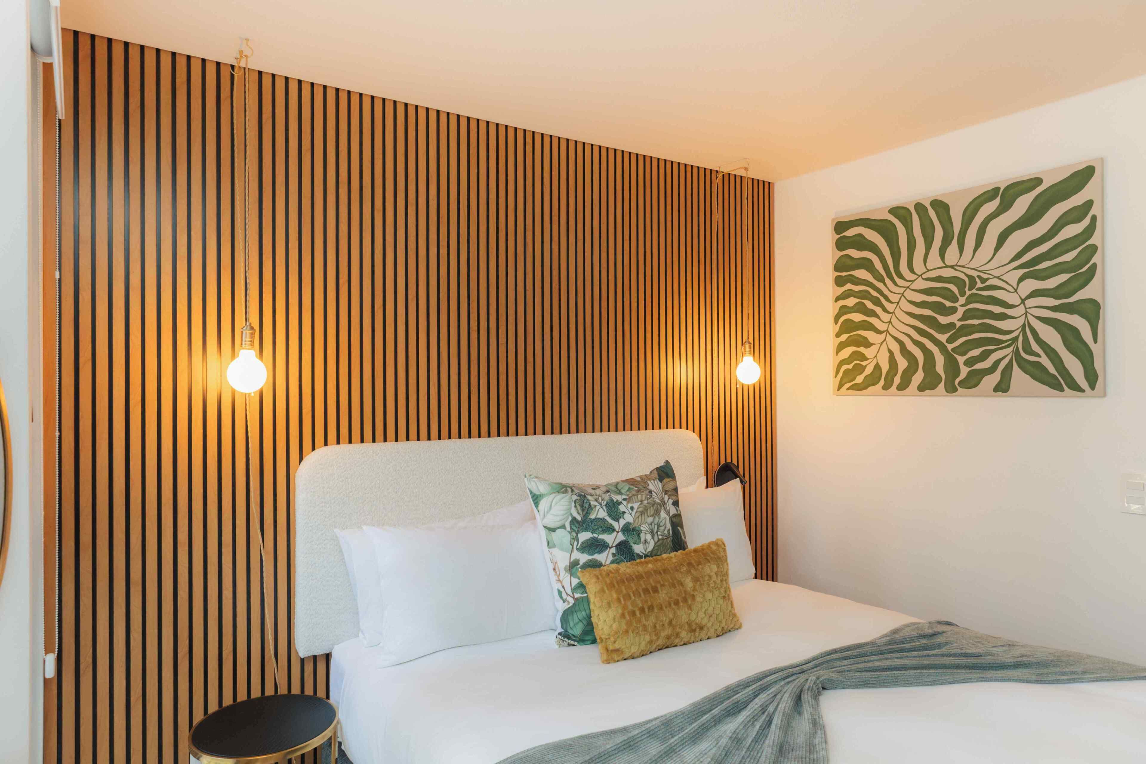 Una cama con cabecera, dos almohadas, una colcha y una lámpara de pared.