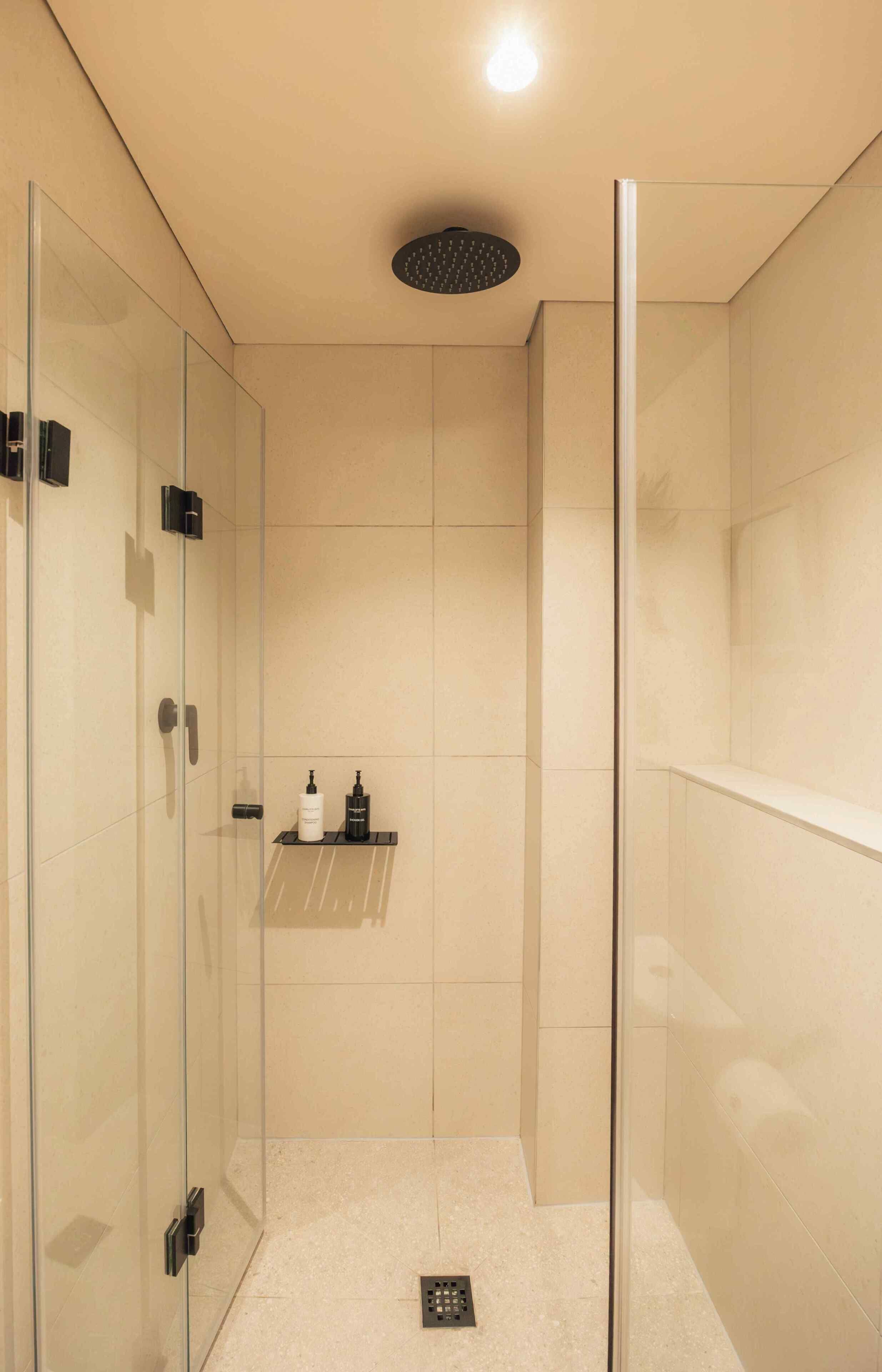A modern shower with a glass door, a shelf with toiletries, and a light fixture on the ceiling.