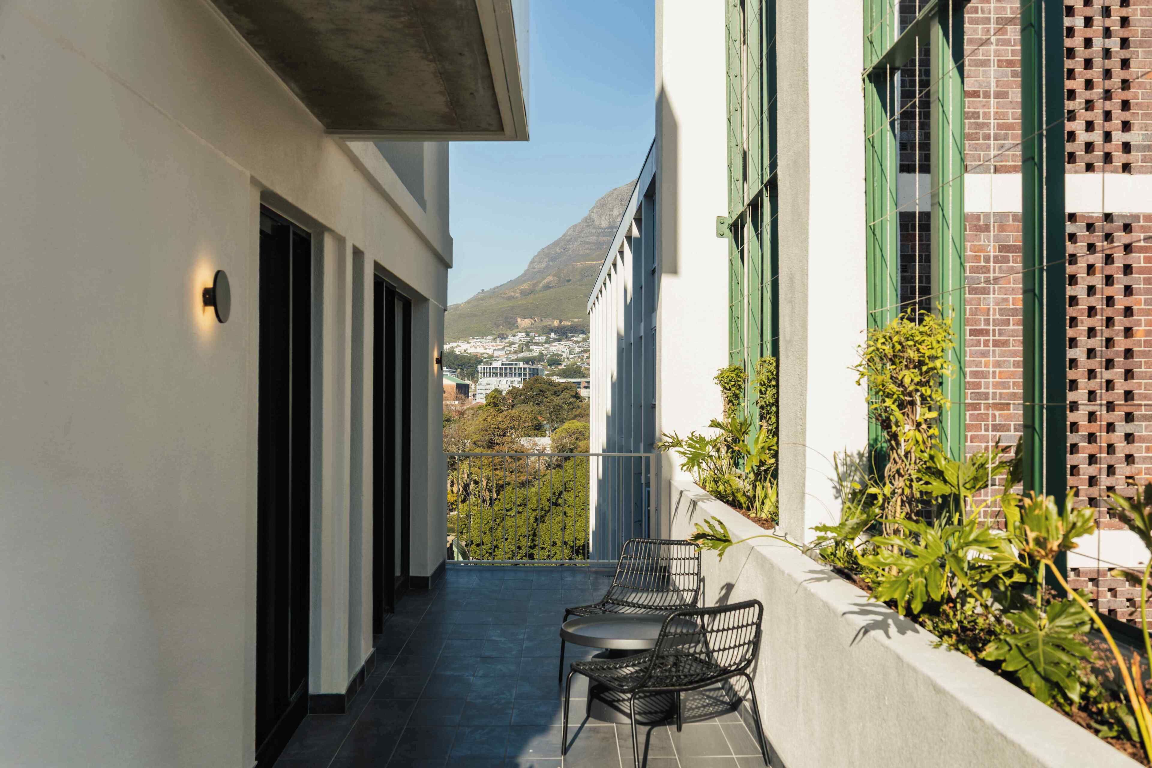 Un balcón con dos sillas y una mesa, con vistas a un paisaje urbano y una montaña al fondo.