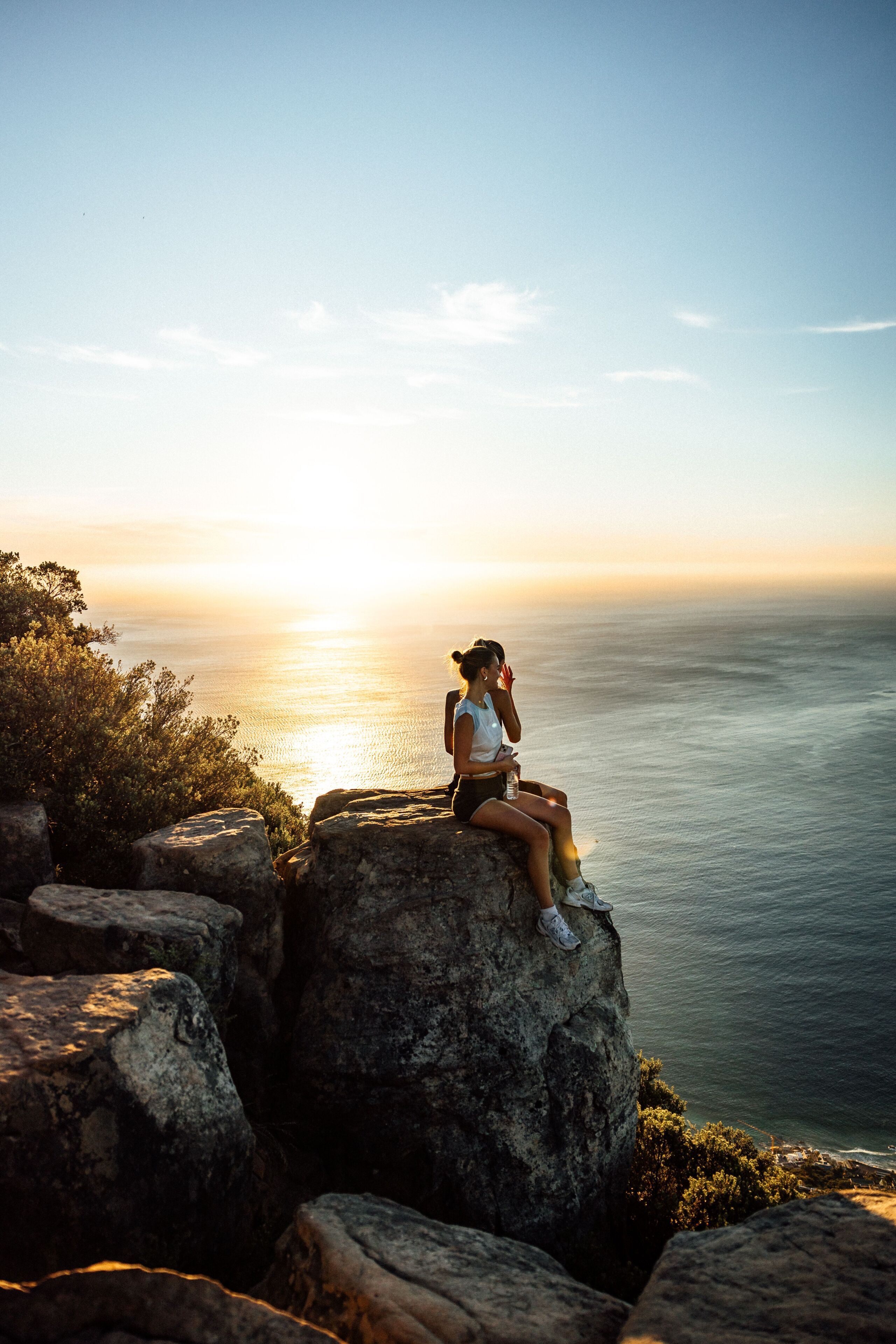 A person sitting on a rock with a view of the ocean and a sunset.