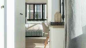 A modern bedroom with a bed, a chair, a bedside table, and a window with a view of a brick building. - TEN on V - Fluent Serviced Apartments (Cape Town)