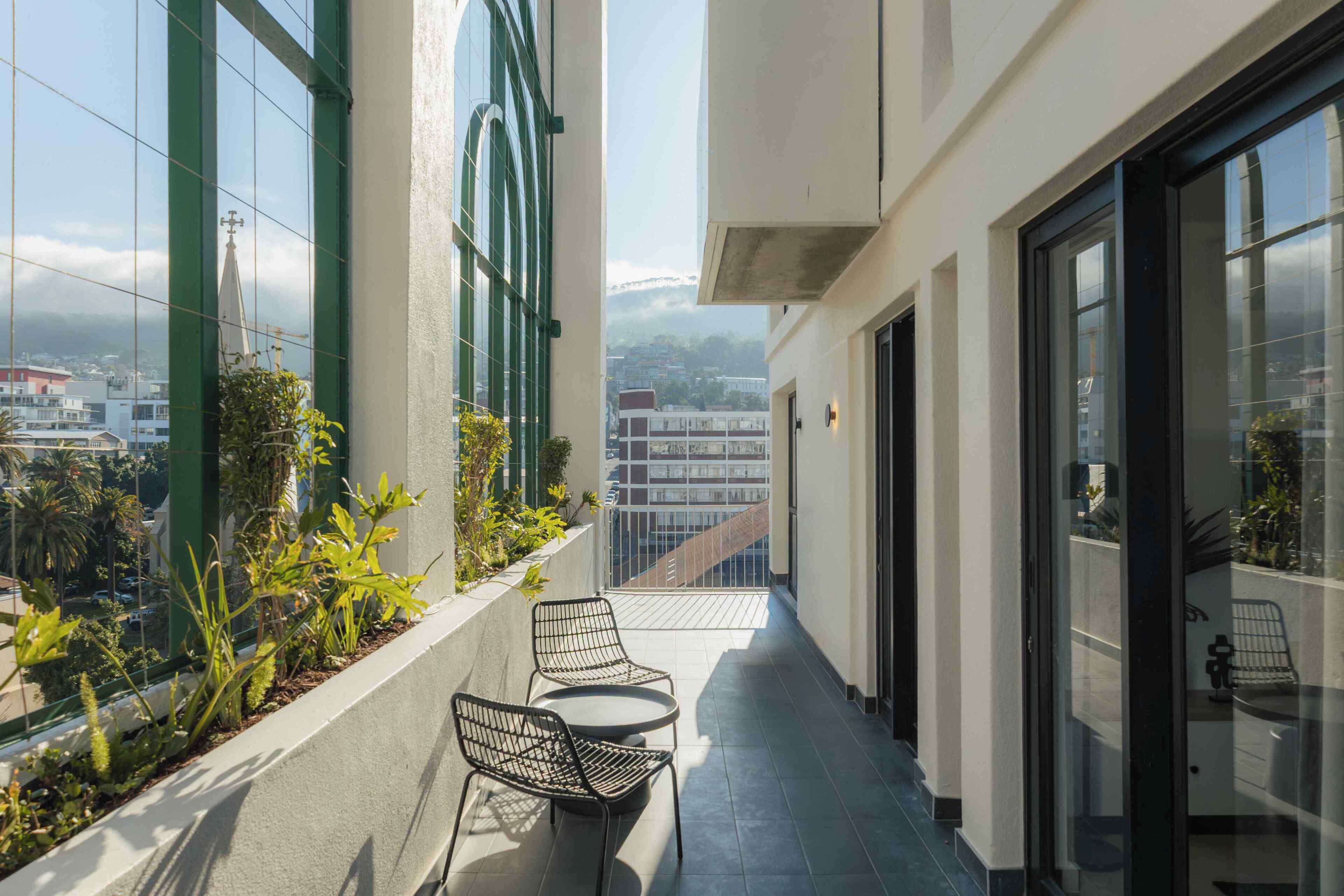 A balcony with a view of a cityscape, a small table with chairs, and a glass door.