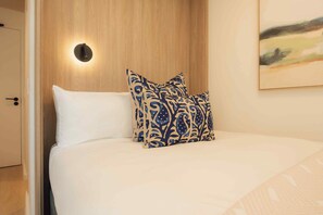 A hotel room with a wooden headboard, a white bed, and a patterned pillow. - TEN on V - Fluent Serviced Apartments (Cape Town)