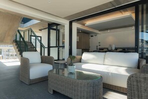 A modern living area with wicker furniture, a glass coffee table, and a view of the outside. - TEN on V - Fluent Serviced Apartments (Cape Town)