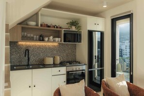 A compact kitchen with a built-in microwave, stove, and oven. There is a sink with a modern faucet, and a countertop with a kettle and toaster. A plant is on the shelf above the microwave. - TEN on V - Fluent Serviced Apartments (Cape Town)